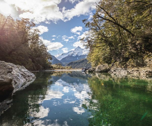 Sunlit stream, green tress and snow-capped mountain peaks in the distance